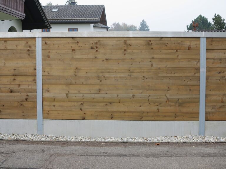 Reflektierende Bohlen-Lärmschutzwand entlang einer Grundstücksgrenze zur Reduzierung von Verkehrs- und Umgebungslärm